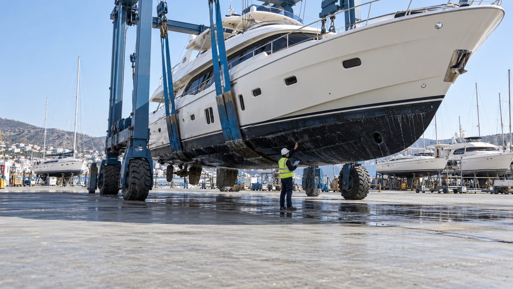 Travel lift ile karaya alınmış bir motoryatın karinasını inceleyen sörveyör